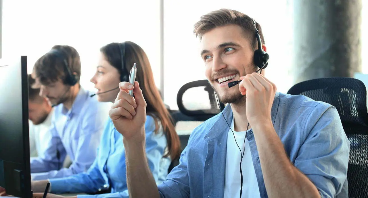 Portrait of call center worker accompanied by his team. Smiling customer support operator at work