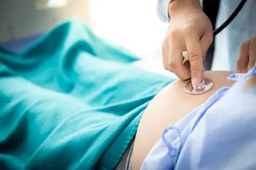 Handsome Doctor or Obstetrician listen fetus heartbeat and check fetus position on mother belly by using stethoscope at hospital room. Mom nearly give birth first child of family. Baby has good health